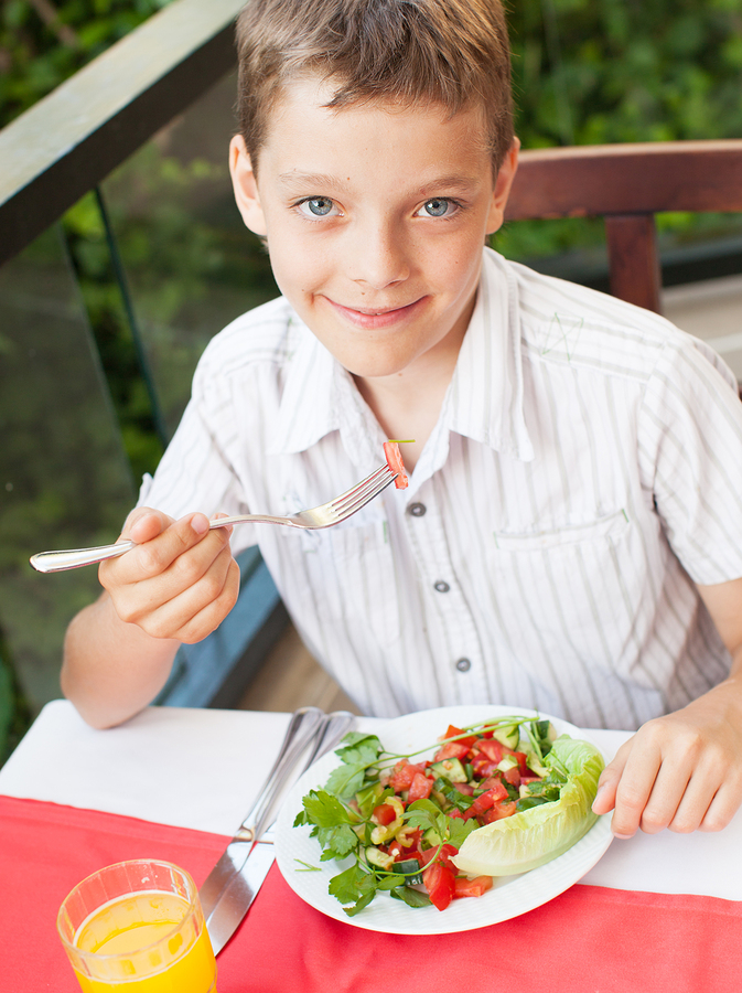 Boy eating salad at a cafe. Teenager eating outdoors